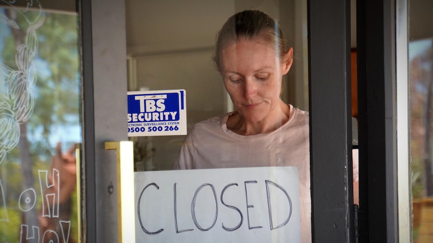 A woman puts a sign on her shop window saying closed.