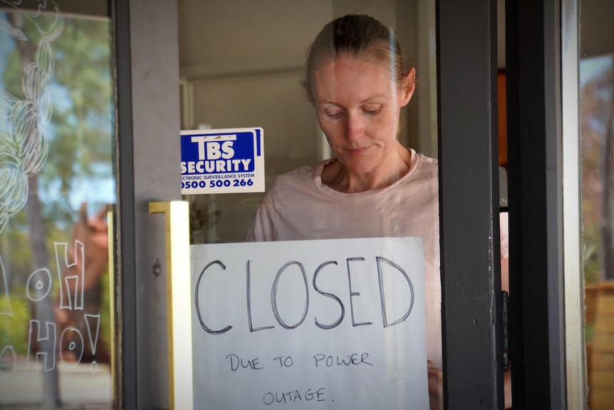 A woman puts a sign on her shop window saying closed.
