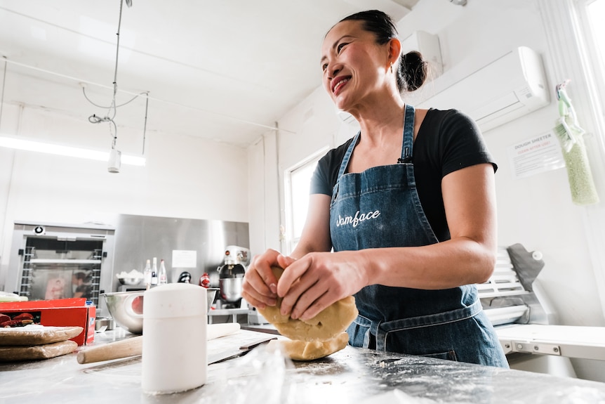 A woman in an apron kneads dough while smiling.