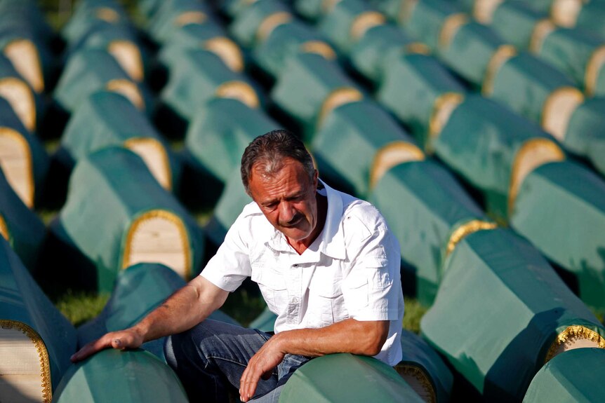 A Bosnian Muslim cries near the coffin with many coffins covered in green behind him