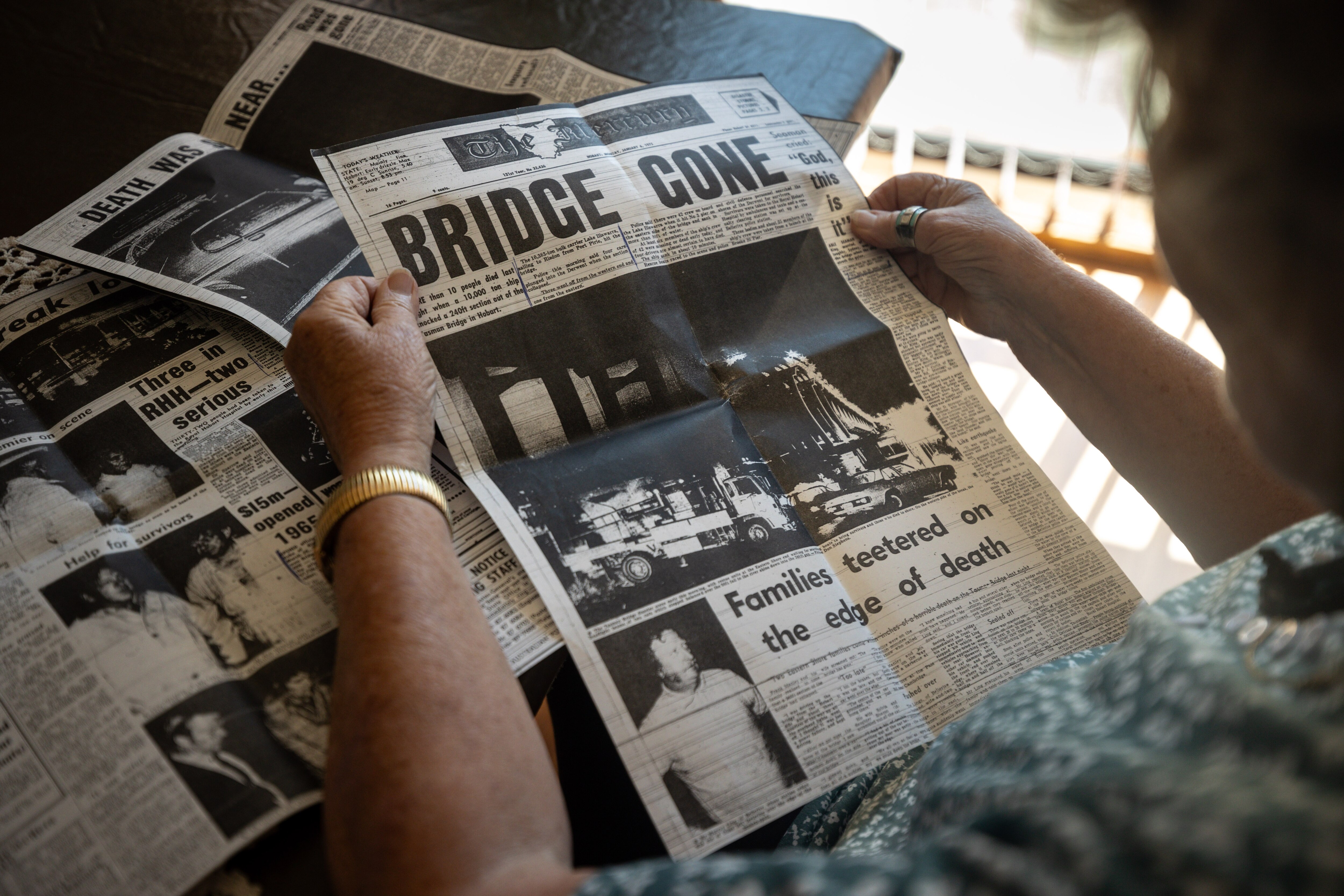 An 80 year old lady in a green looking at a historical newspaper clipping.