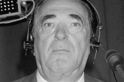 Robert Maxwell wearing headphones and near a microphone stares down the camera.