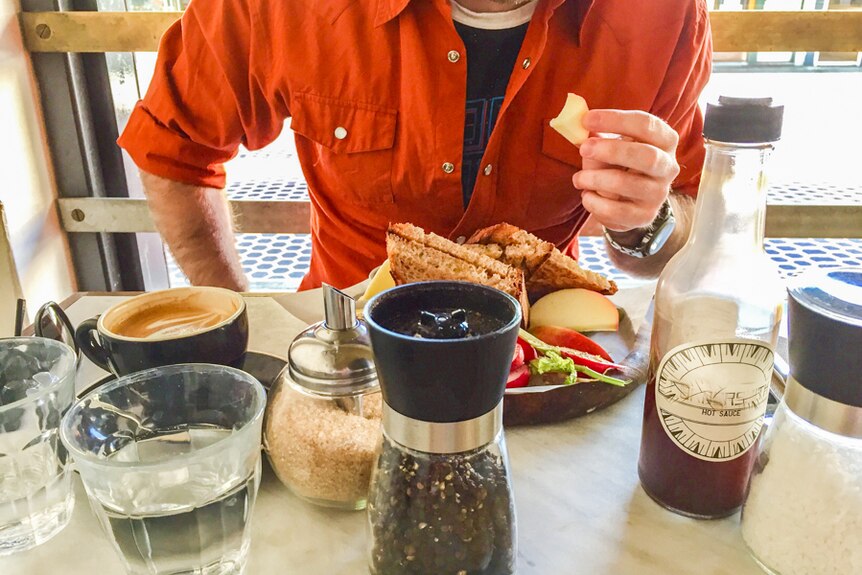 A man eating a meal in a cafe with a cup of coffee.