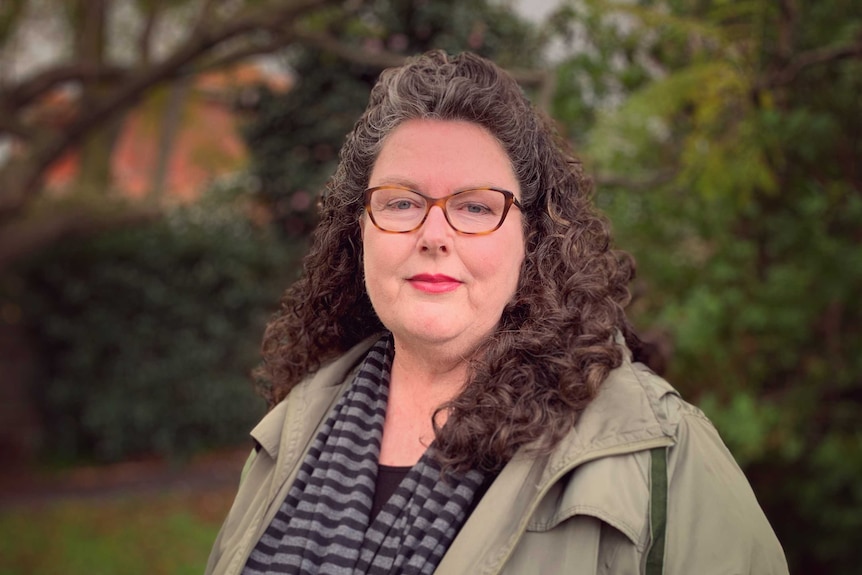 A portrait shot of a woman with a beige jacket, brown hair and glasses.