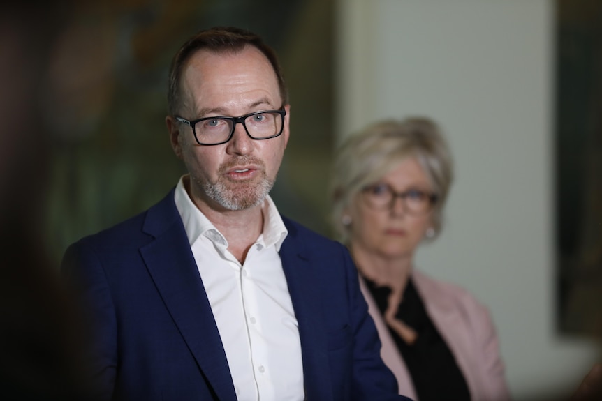 Senator Shoebridge wears black glasses, a white shirt and a navy blazer. 