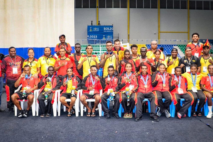 More than 20 boxers from Papua New Guinea are lined up in two rows, posing for a team photo, wearing medals.
