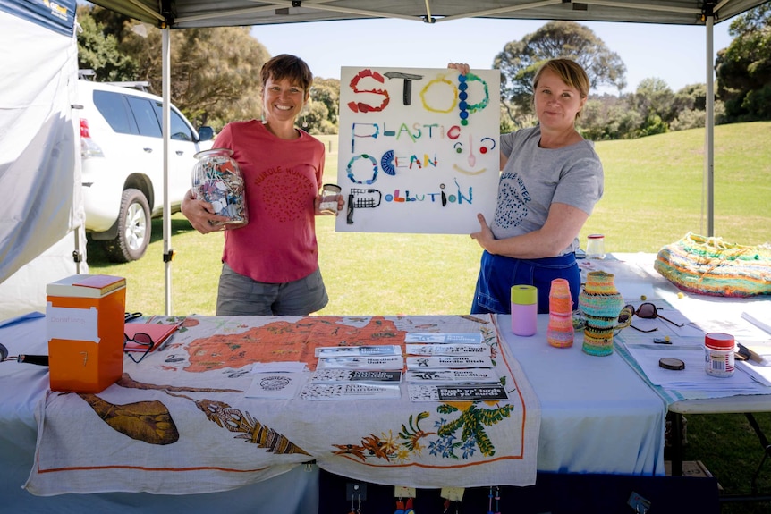 Colleen Hughson wearing pink shirt and holding sign that says 'stop plastic ocean pollution' with another woman.