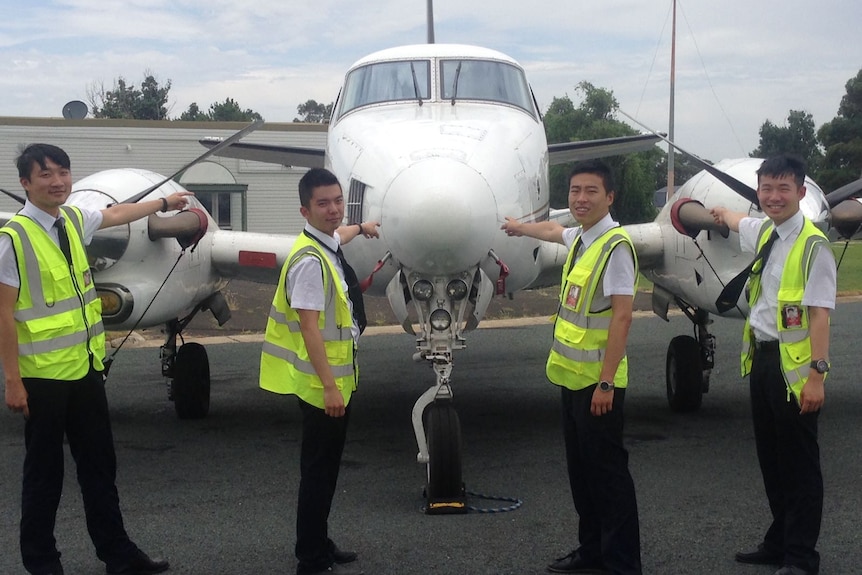 Four students standing in front of an airplane on the tarmac at airport