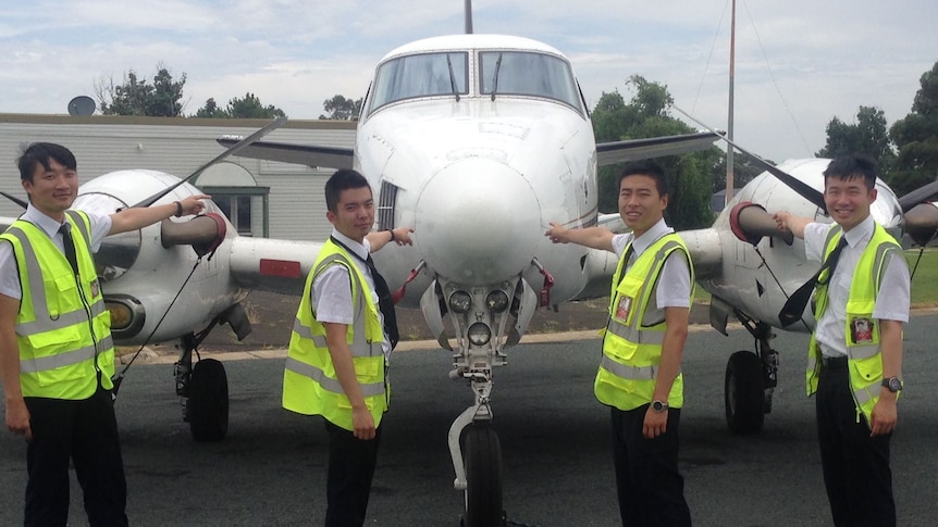 Four students standing in front of an airplane on the tarmac at airport