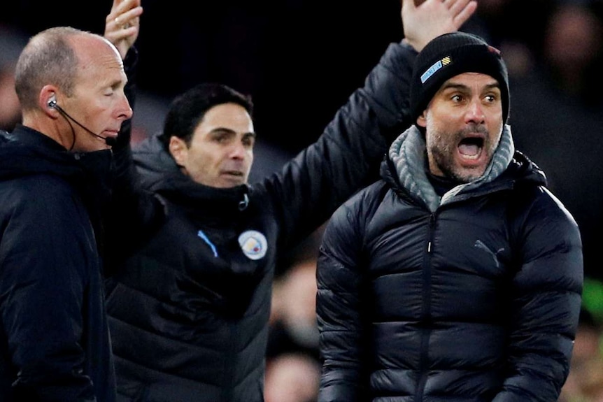 Manchester City Pep Guardiola shouts at the fourth official. An assistant stands behind him with his arms in the air.