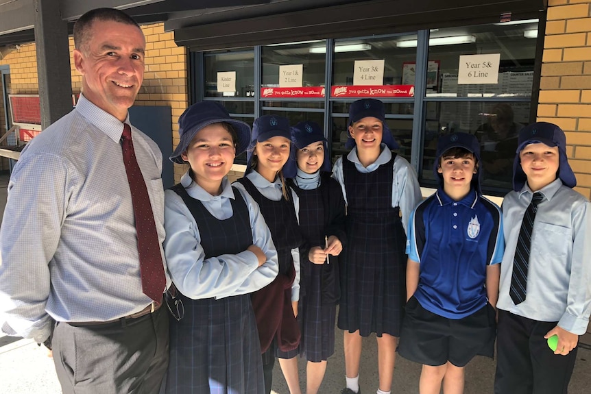 The principal Matt smiles alongside six students, including Ronan Marc, in the grounds of their school.