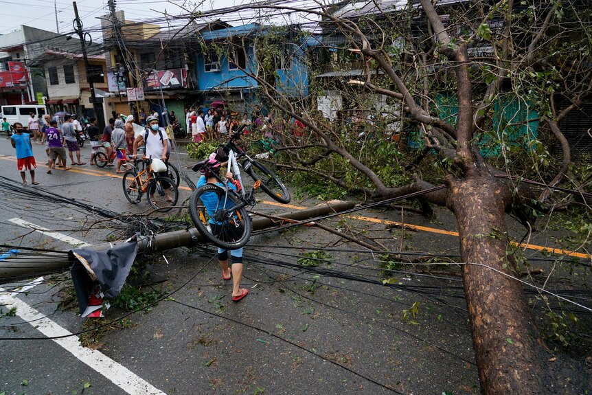 A resident carries bicycle over the toppled electrical post and tree caused by Typhoon Rai in Cebu city.
