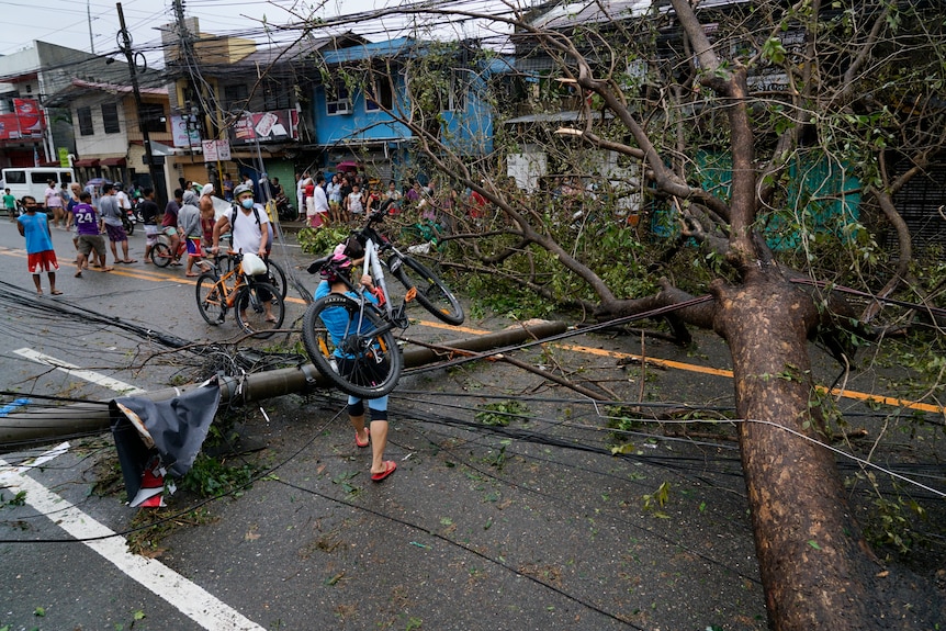 宿务市一名居民携带自行车越过因飓风雷造成倒塌的发电站和树木。