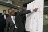 Medium shot of a man in a suit pointing to a diagram of a human body.