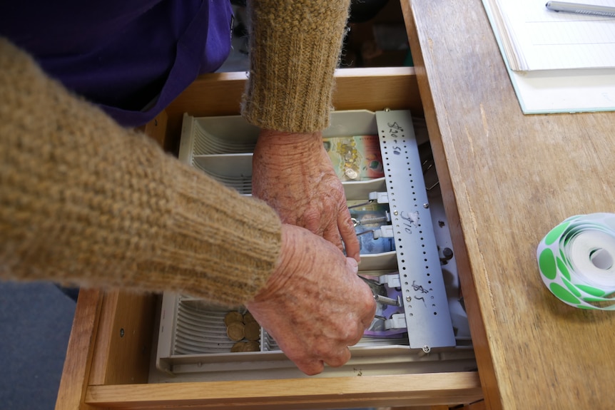 Hands reaching into a cash register filled with money