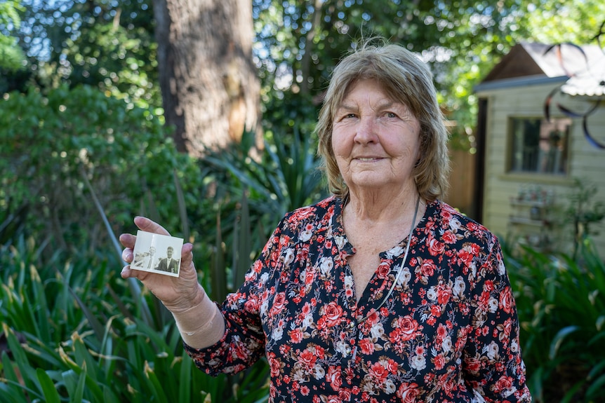 A woman holds a small photograph to the camera.