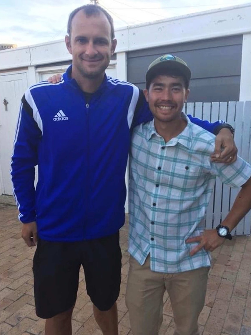 Two men with arms around each other smile to camera.