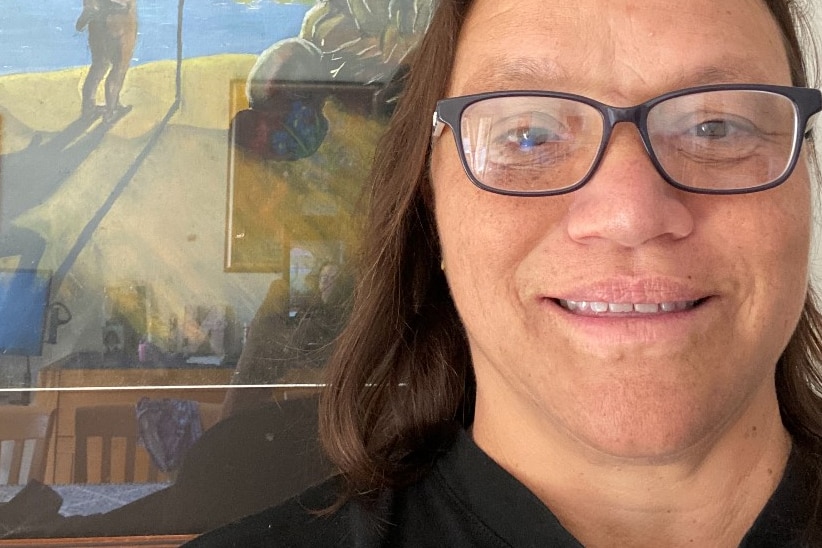 a woman in glasses smiling in front of an Indigenous painting