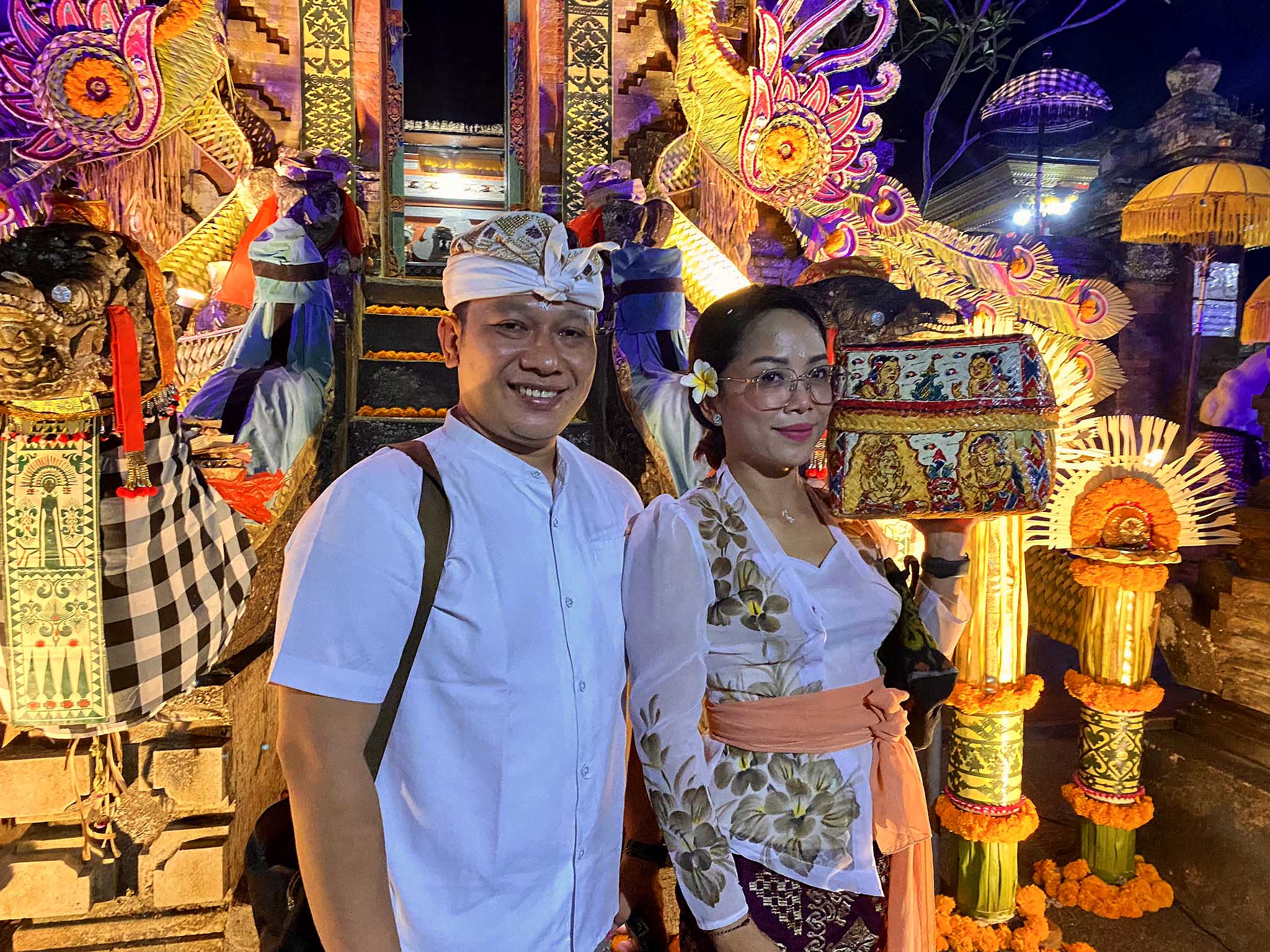 A man and woman in traditional Balinese dress stand outside a temple