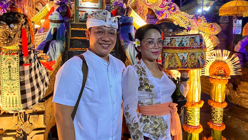 A man and woman in traditional Balinese dress stand outside a temple