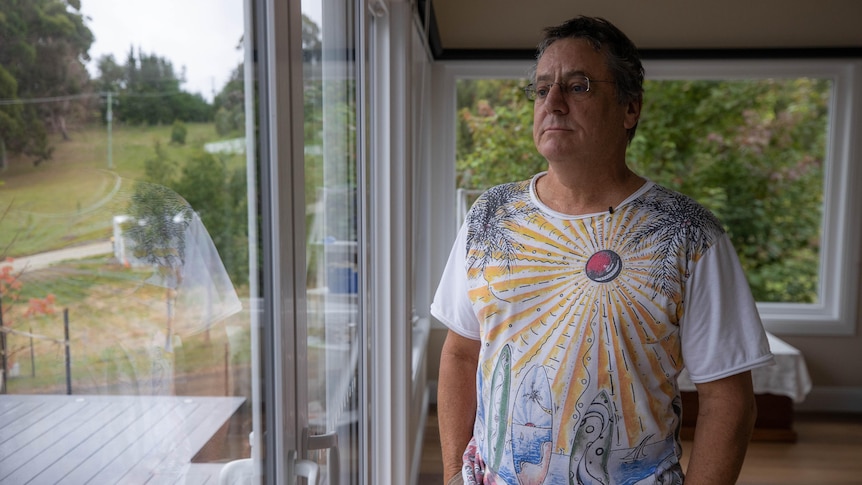  A man stands in a house and looks out a window