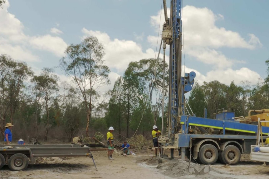 Workers in high-vis attend to drilling equipment.