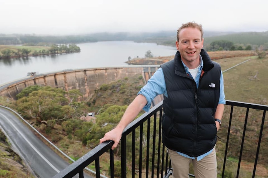 A man wearing a puffy vest standing in front of a reservoir