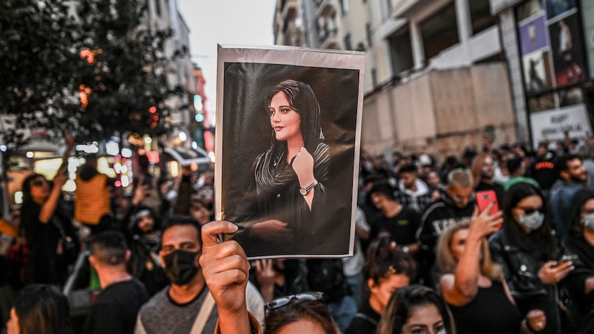 packed protesters with one holding a close up image of mahsa amini