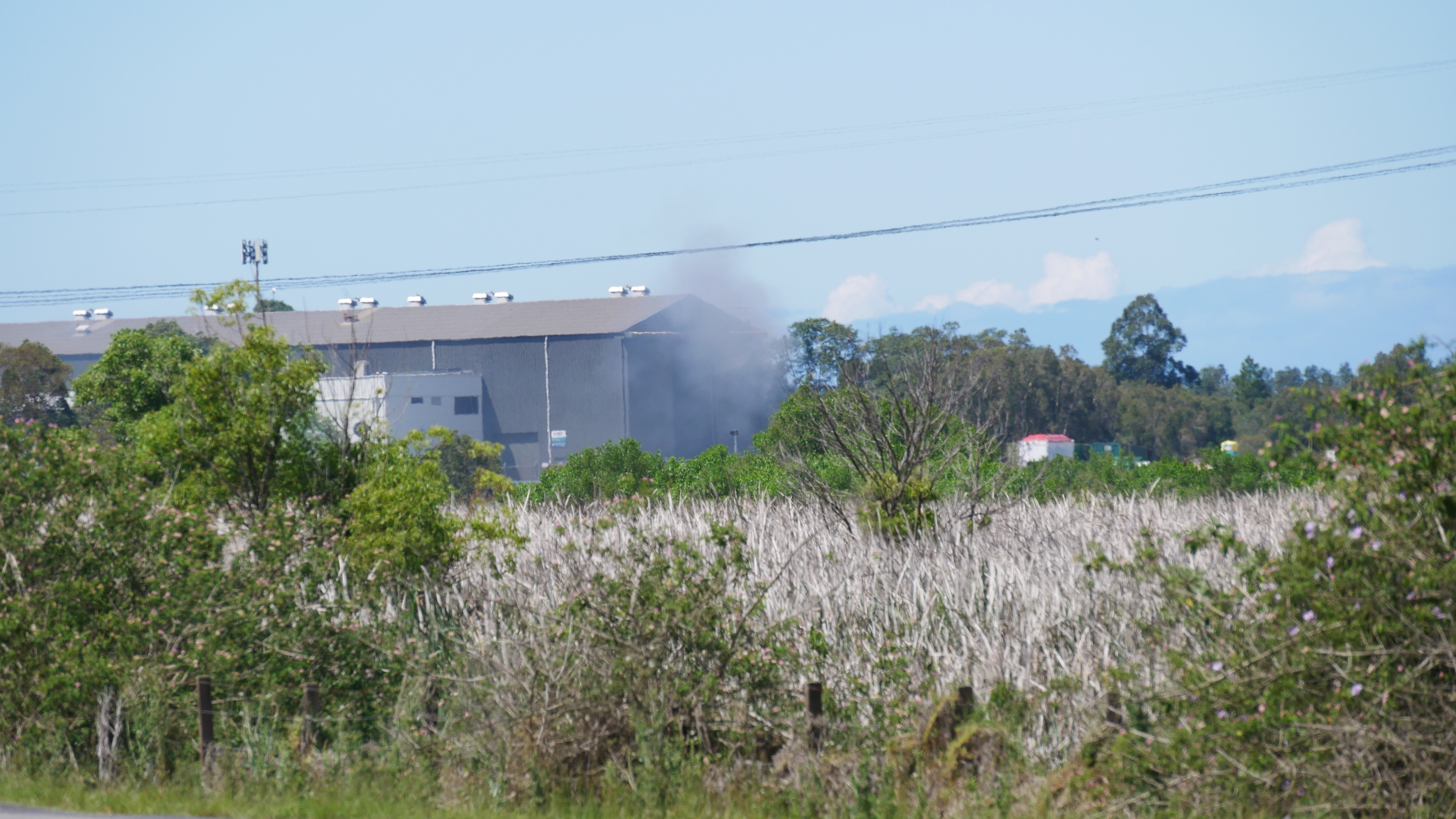 A wide shot of a warehouse with smoke billowing from the site