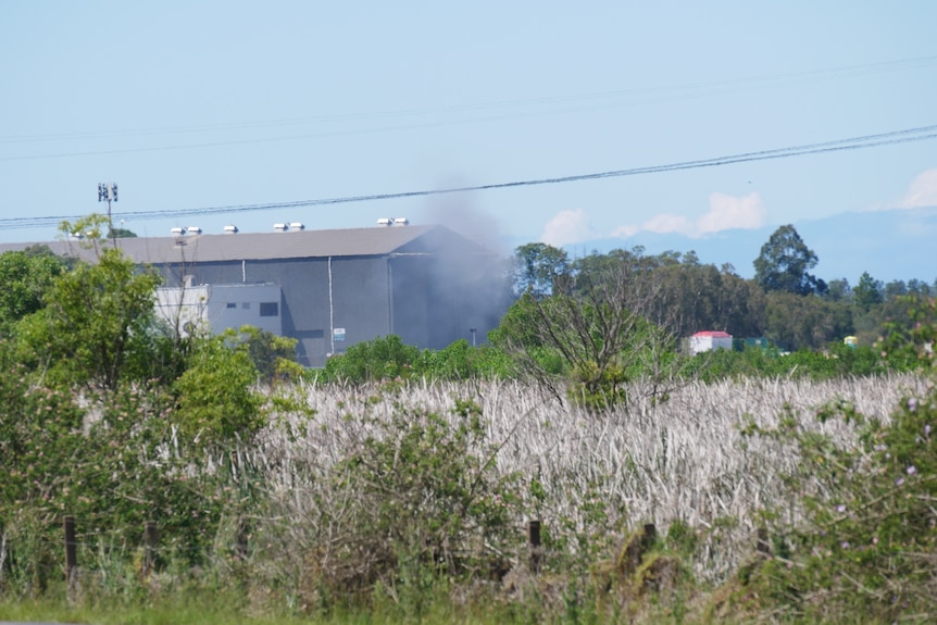 A wide shot of a warehouse with smoke billowing from the site