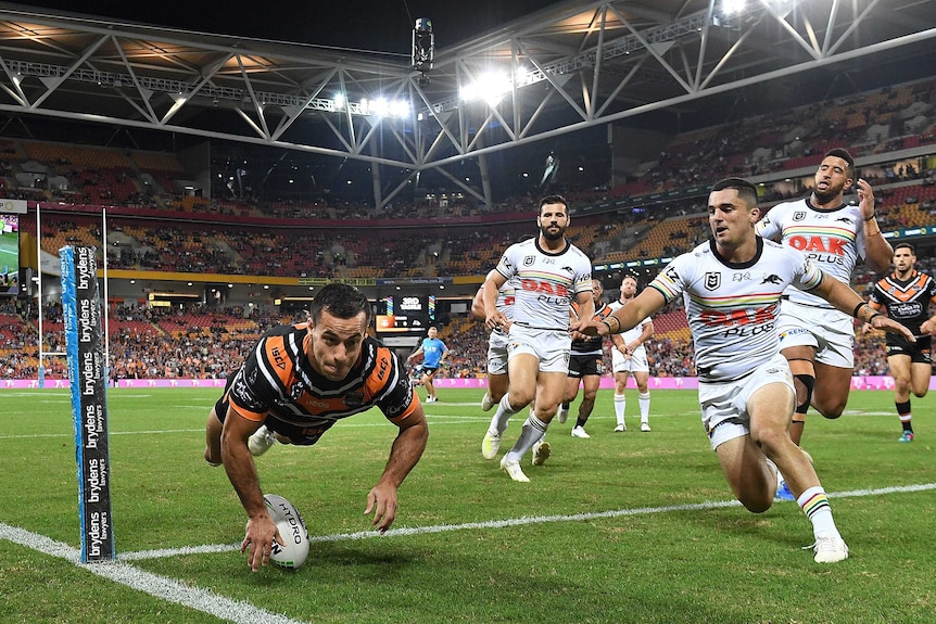 An NRL player touches the ball down in the corner as opposition players watch on.