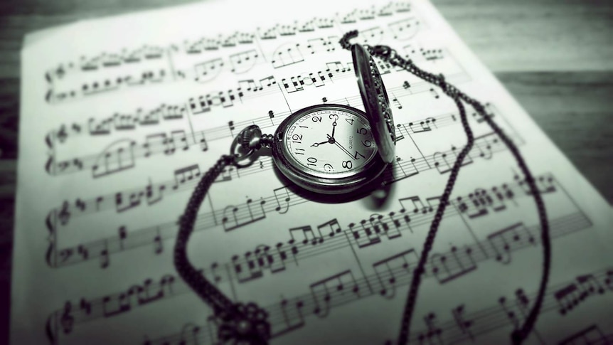 A black and white image, an old pocket watch rests on some piano sheet music.