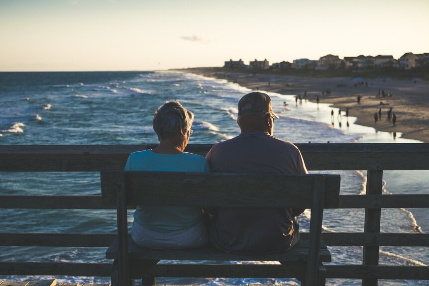 Older couple sitting on a bench overlooking a beach in the golden light.