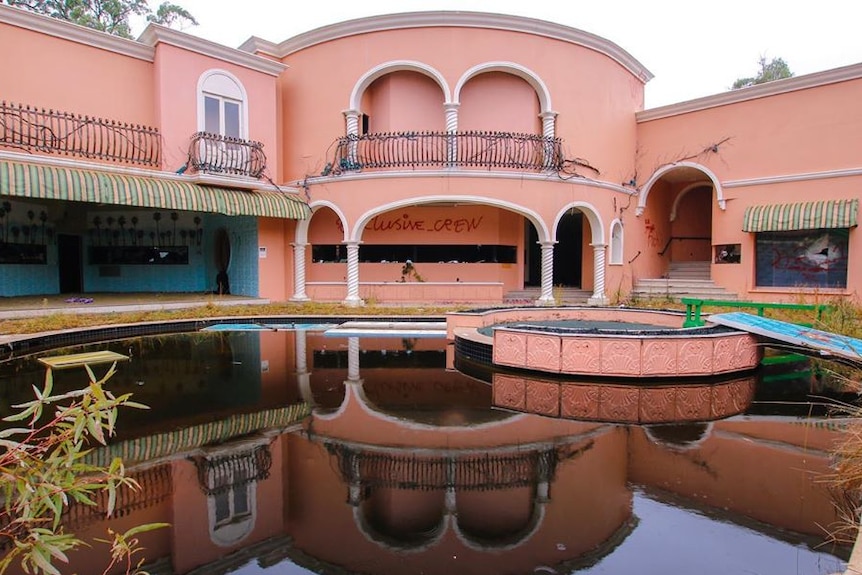 A pink and white house with a stagnant pool.