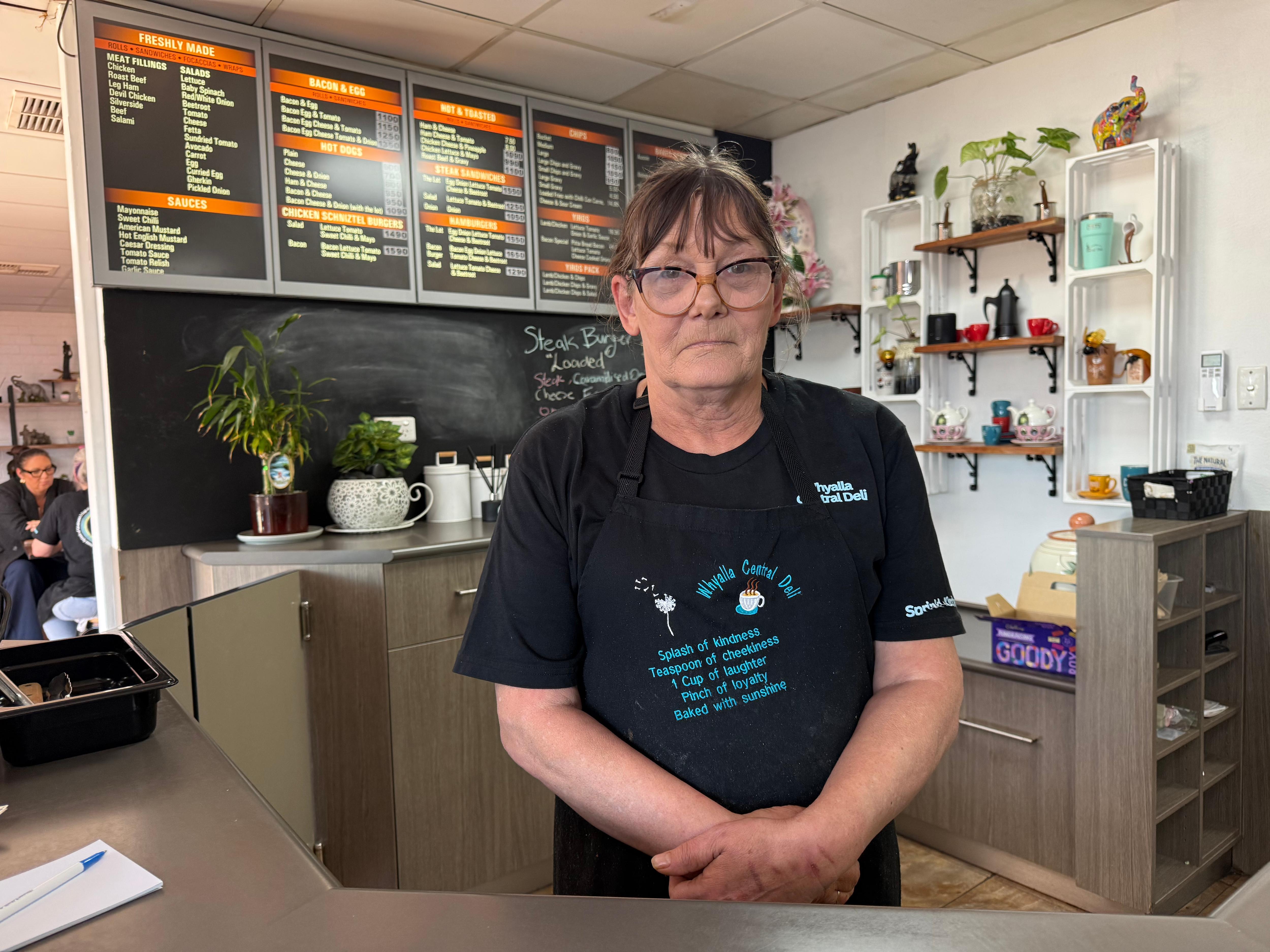 A woman wearing an apron and glasses is standing behind the counter in a cafe