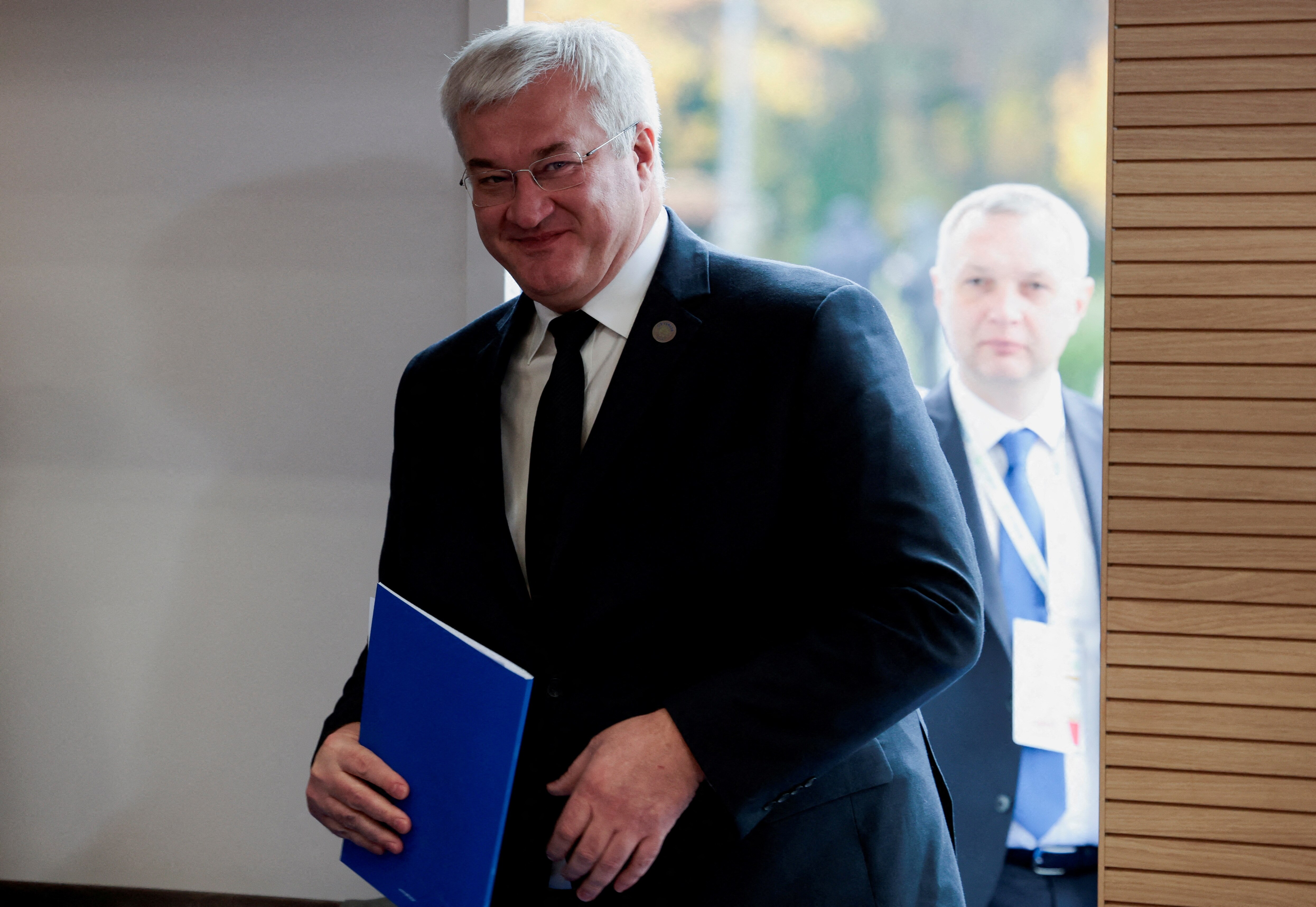 Andrii Sybiha in a suit holding a blue pamphlet. 
