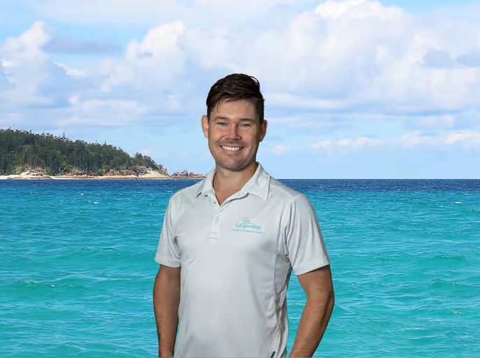 A man wearing a polo shirt smiling at the camera, with water in the background