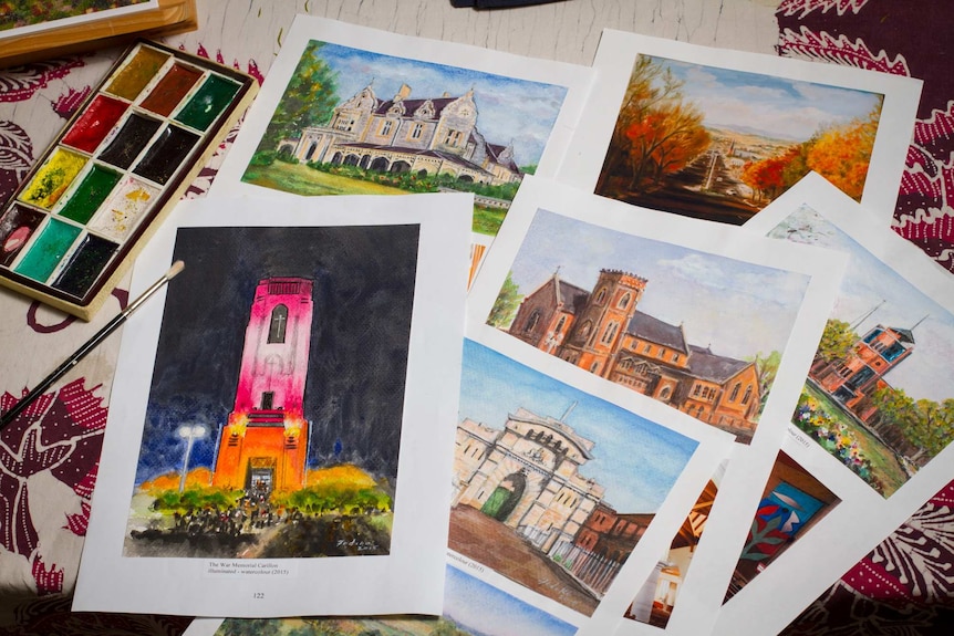 Artworks in watercolour mainly of buildings lying on a table with paints and a brush nearby