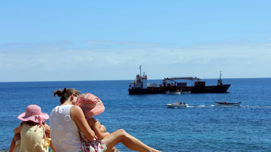 A family watches as a ship is unloaded off the coast of Norfolk Island.