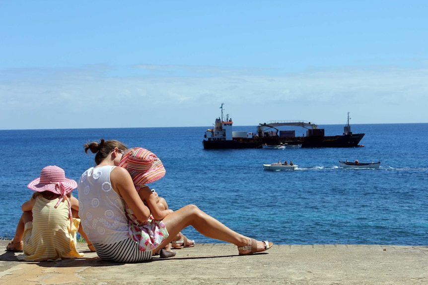 A family watches as a ship is unloaded off the coast of Norfolk Island.