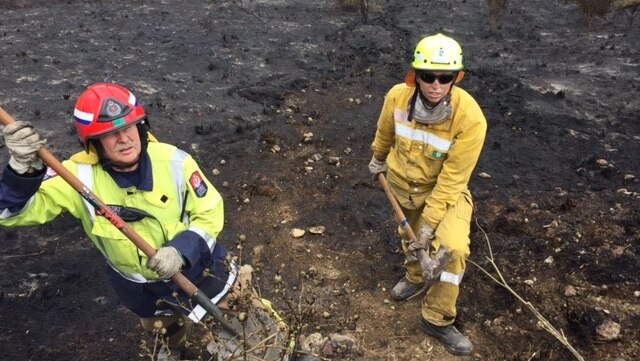 Two firefighters hold a pick axe and a shovel in a burnout field.