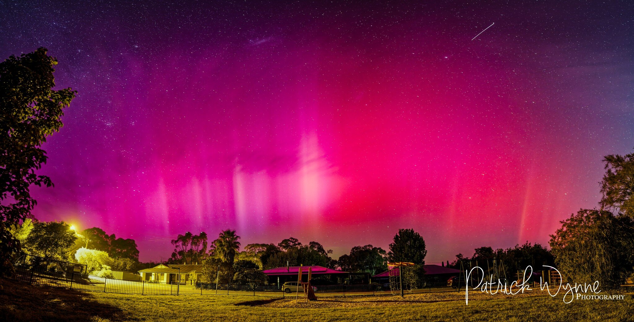 A photo of a bright pink and red aurora in the night sky over someone's house