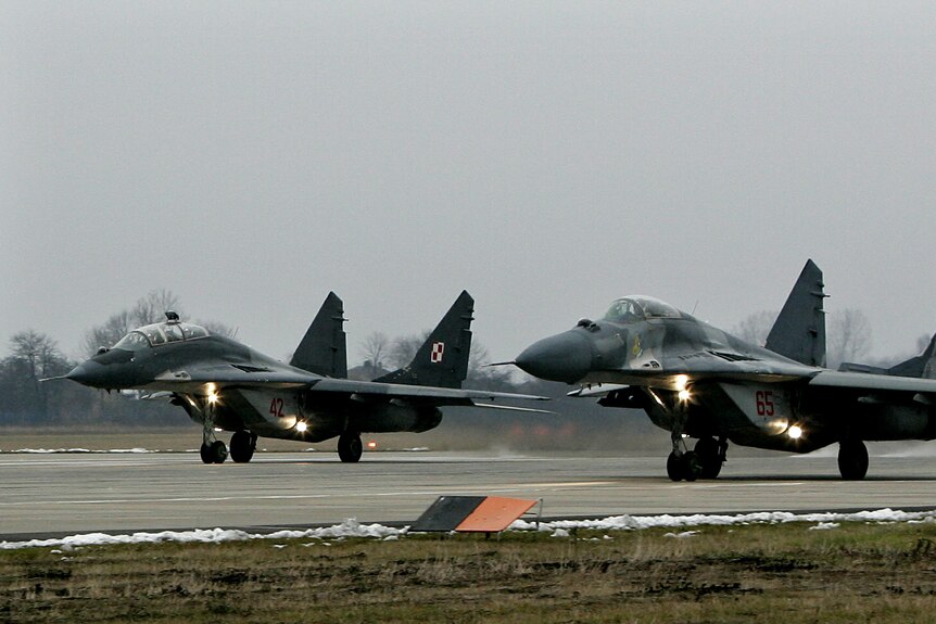Two dark strike jets lift noses off the runway as they launch into flight for a mission.