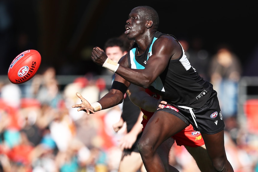 A Port Adelaide AFL player handballs with his left hand against Gold Coast Suns.