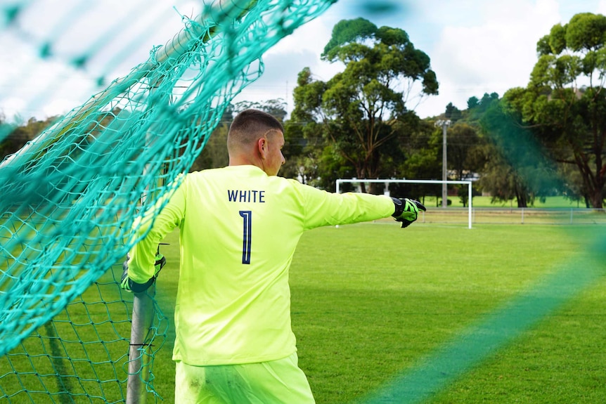 A teenage boy in a bright neon green goalkeeper kit points directions from the goals.