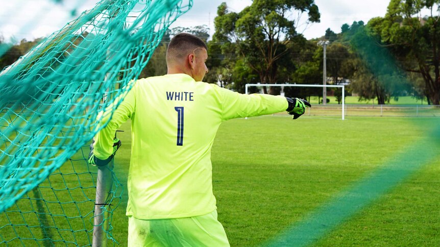 A teenage boy in a bright neon green goalkeeper kit points directions from the goals.