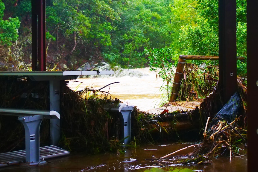 debris and broken fence with rushing flood waters in background