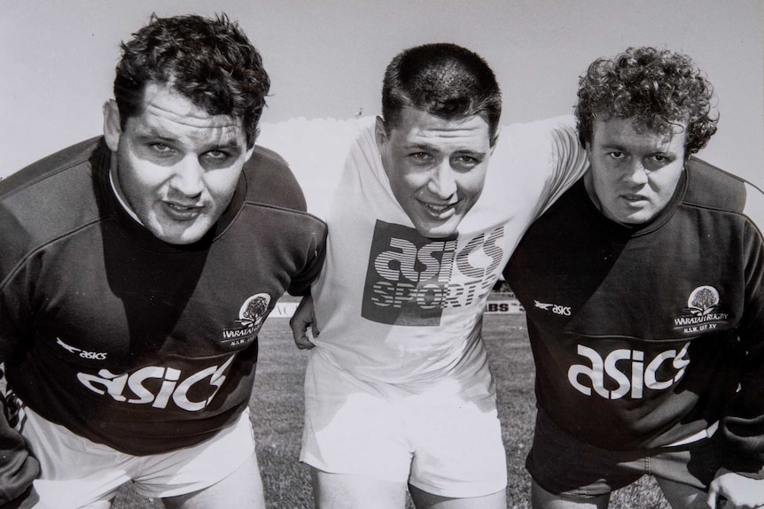 Three men bend down to look at the camera during rugby union training.