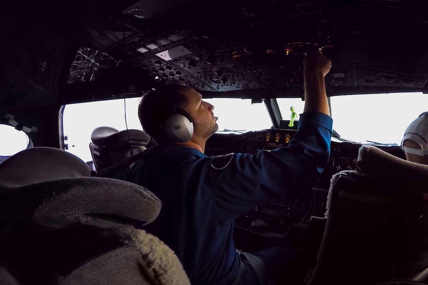 A pilot in a cockpit adjusting buttons.