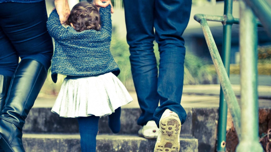 Two parents hold the hands of a toddler.